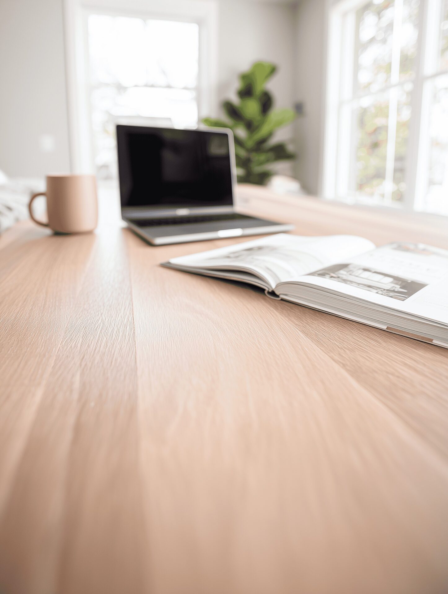 A mug, a laptop, an open book on a beautiful wood table